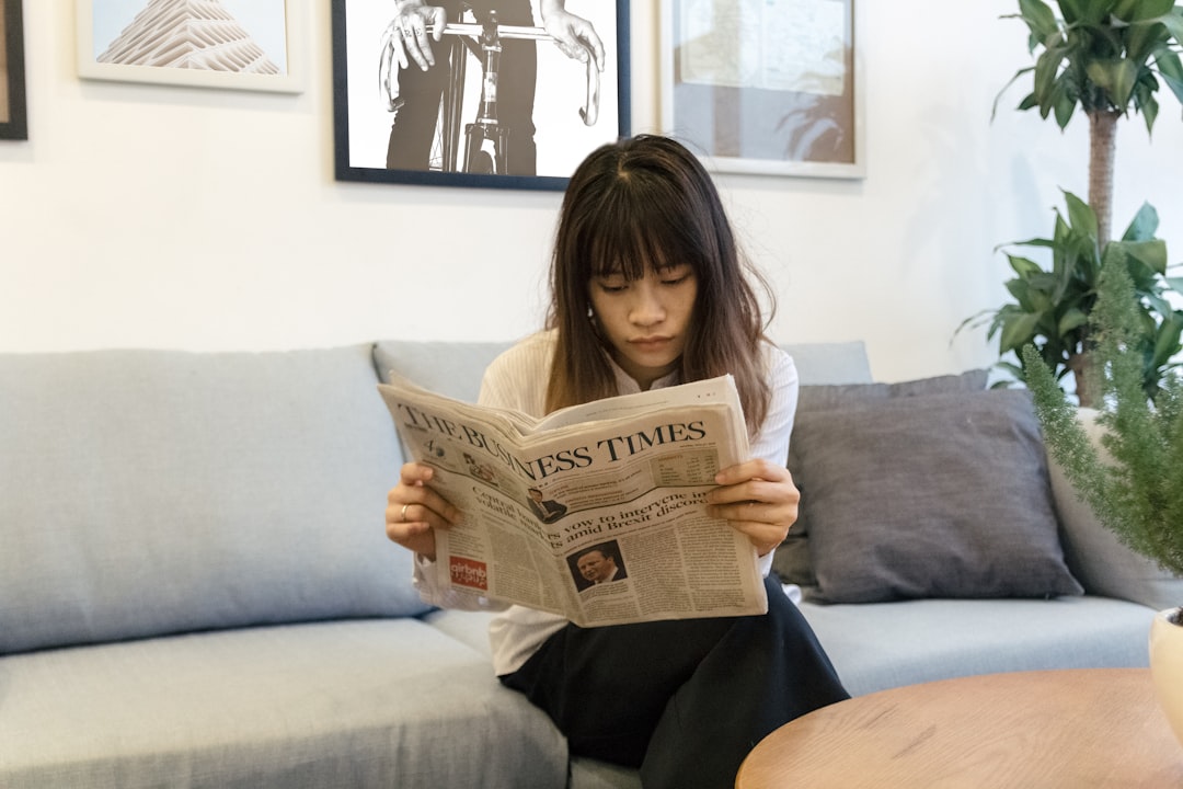 a-woman-sitting-on-a-couch-reading-a-newspaper-b0utrei7vfc